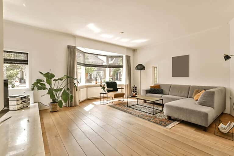 a living room with hardwood flooring and white walls there is a grey couch in front of the gray sofa